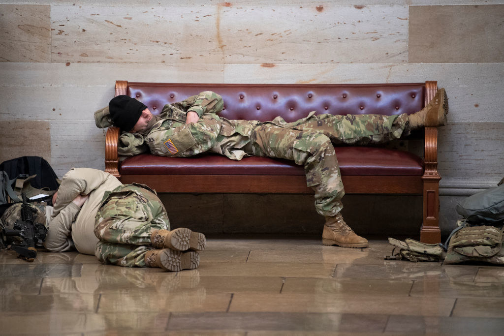 A National Guardsman lies on a bench with their hat over their eyes