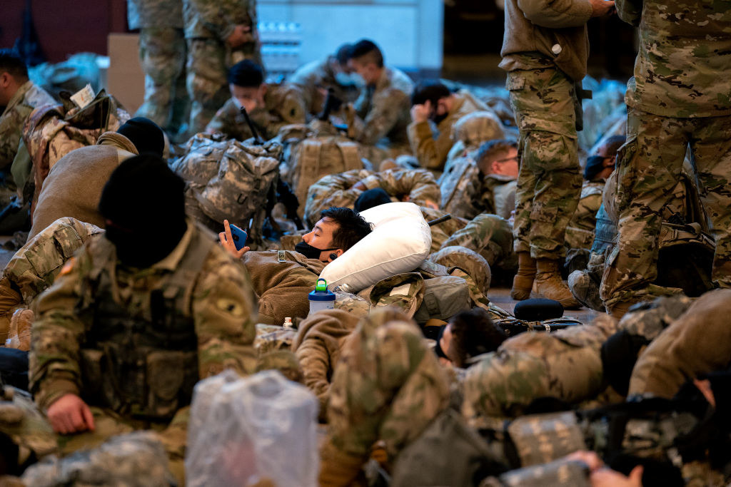 A National Guard member lies on a pillow as he looks through his phone in the Capitol