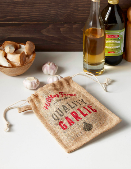 A jute garlic bag on a kitchen counter with several heads of garlic peeking out