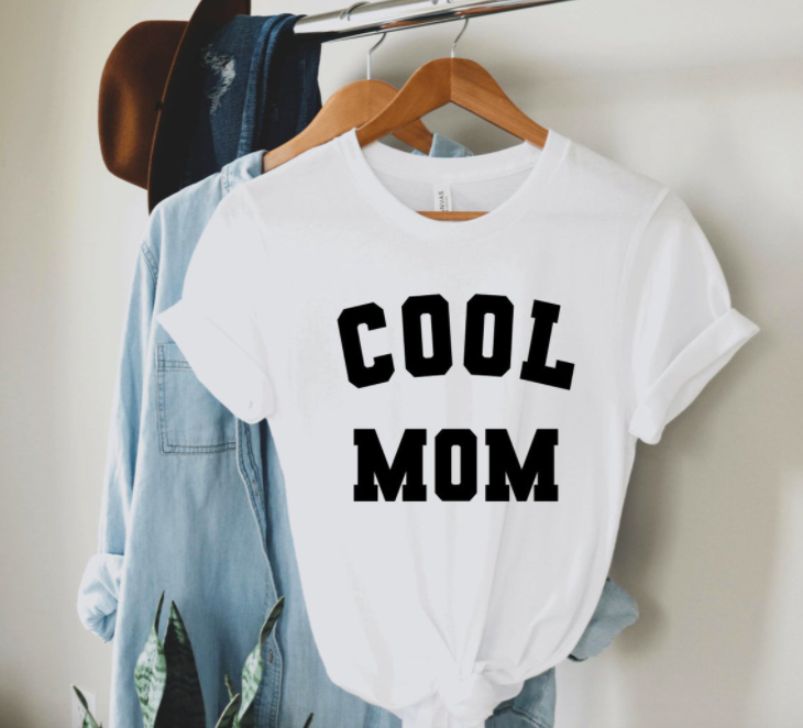 A simple tee shirt hung on a rack with the words cool mom printed on the front in large block letters