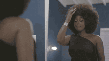 A woman with natural hair touches up her afro in the mirror