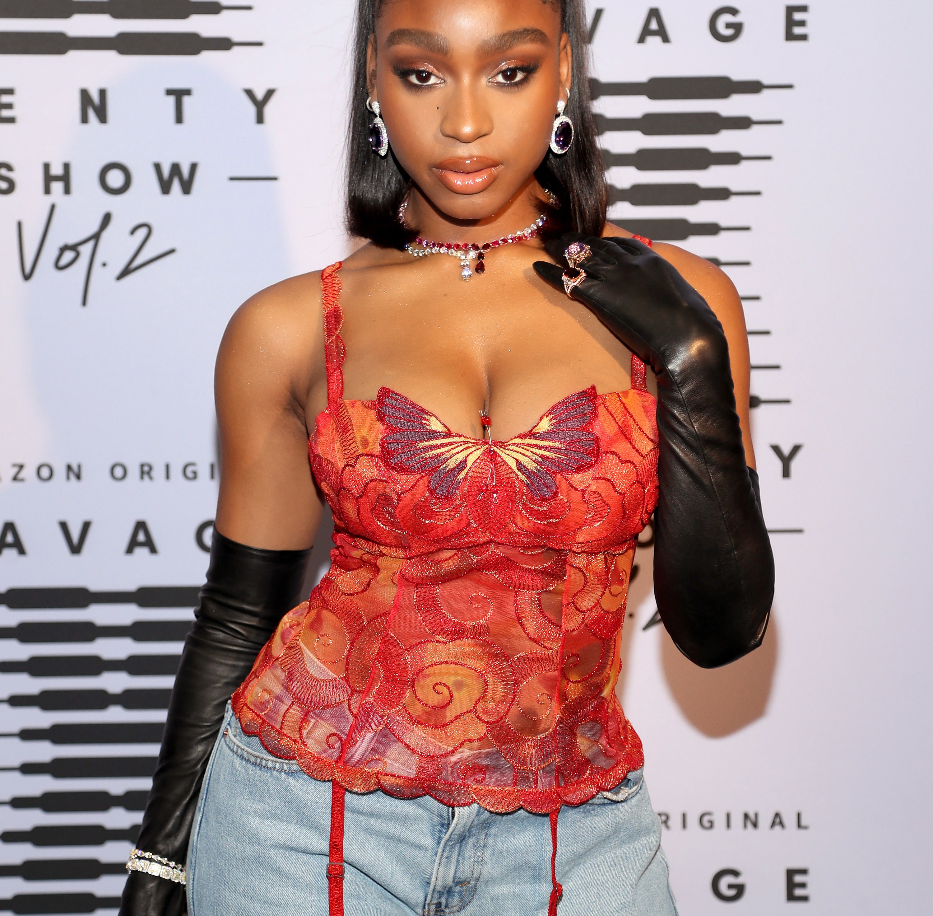 Normani on a red carpet with a red top and long black leather opera gloves