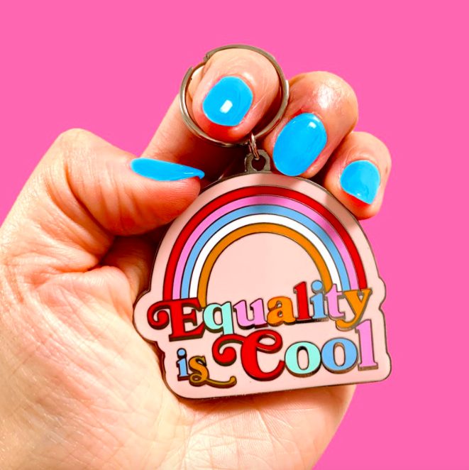A person holding a colourful keychain with the words equality is cool on it
