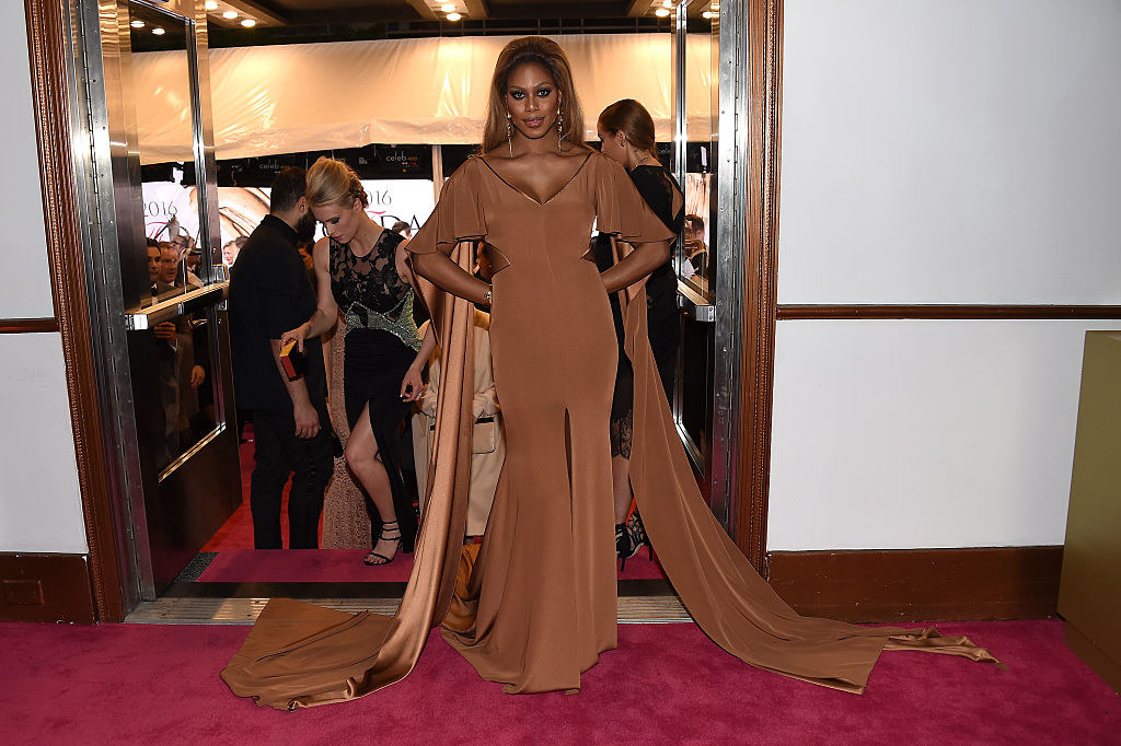 Laverne in a silky dress with elbow-length fluttery sleeves, a wide V neck, a slight mermaid flare at the bottom, and a cape behind her shoulders