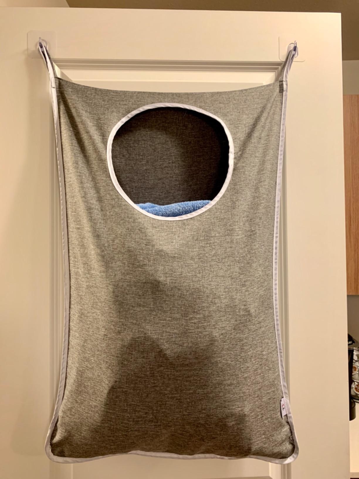 reviewer image of the grey laundry hamper bag hanging over top of door filled with laundry