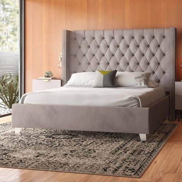 The bed frame in gray, with a tall headboard with tufting and slightly forward-curved, wingback-style edges