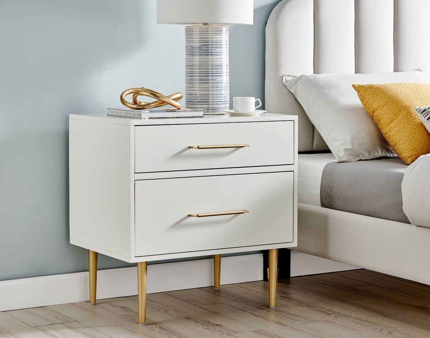 A white two drawer nightstand with brass handles and legs
