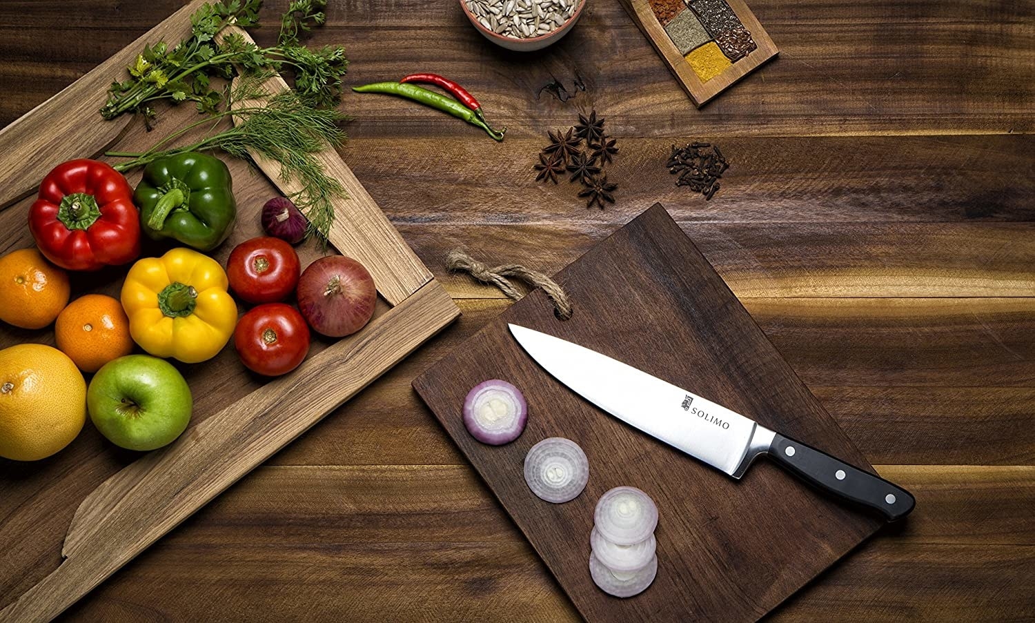 A chef&#x27;s knife with various fruits and vegetables near it 