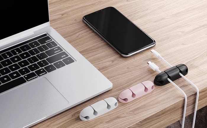 Three cable holders on a desk with wires running through one of them, next to a laptop and a phone