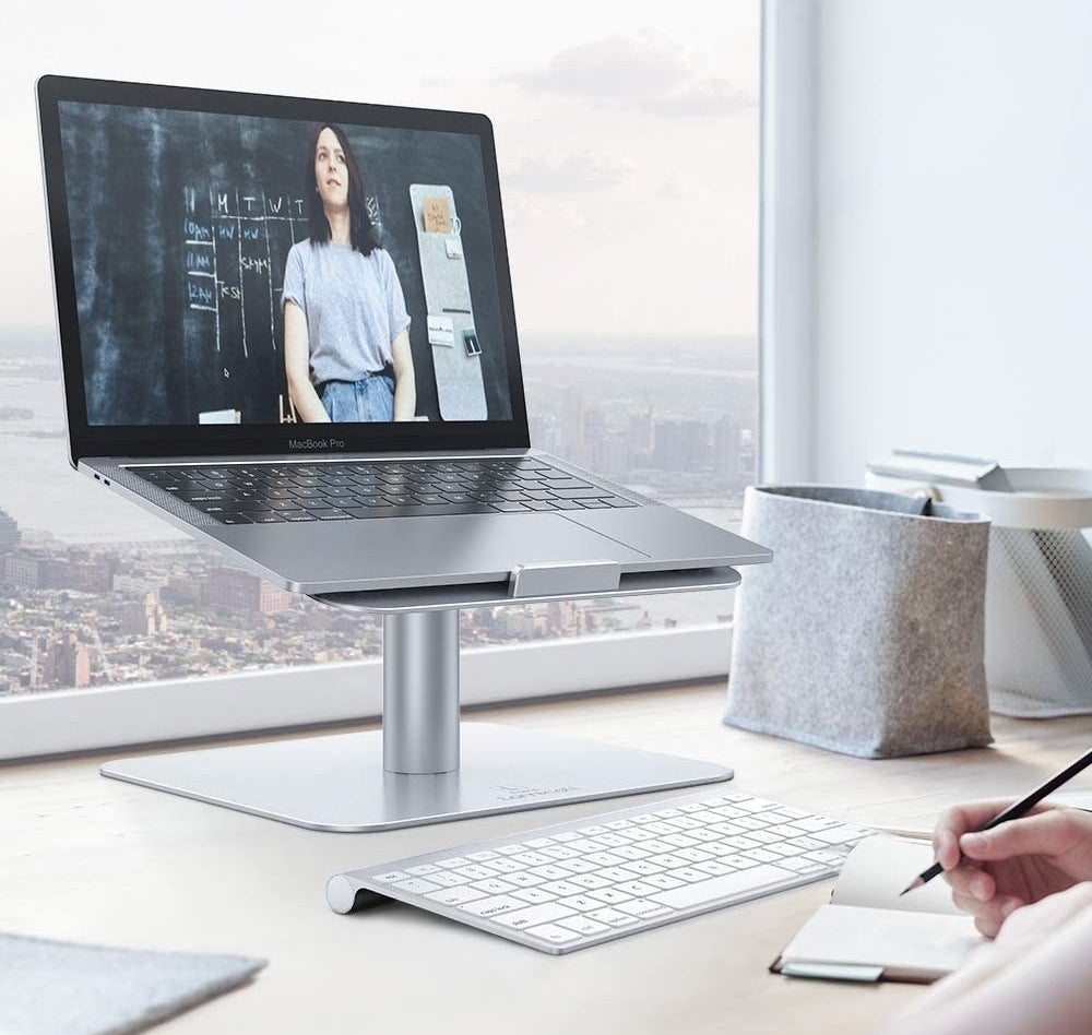 A laptop on the swivel stand in front of a large window with a separate keyboard beneath it