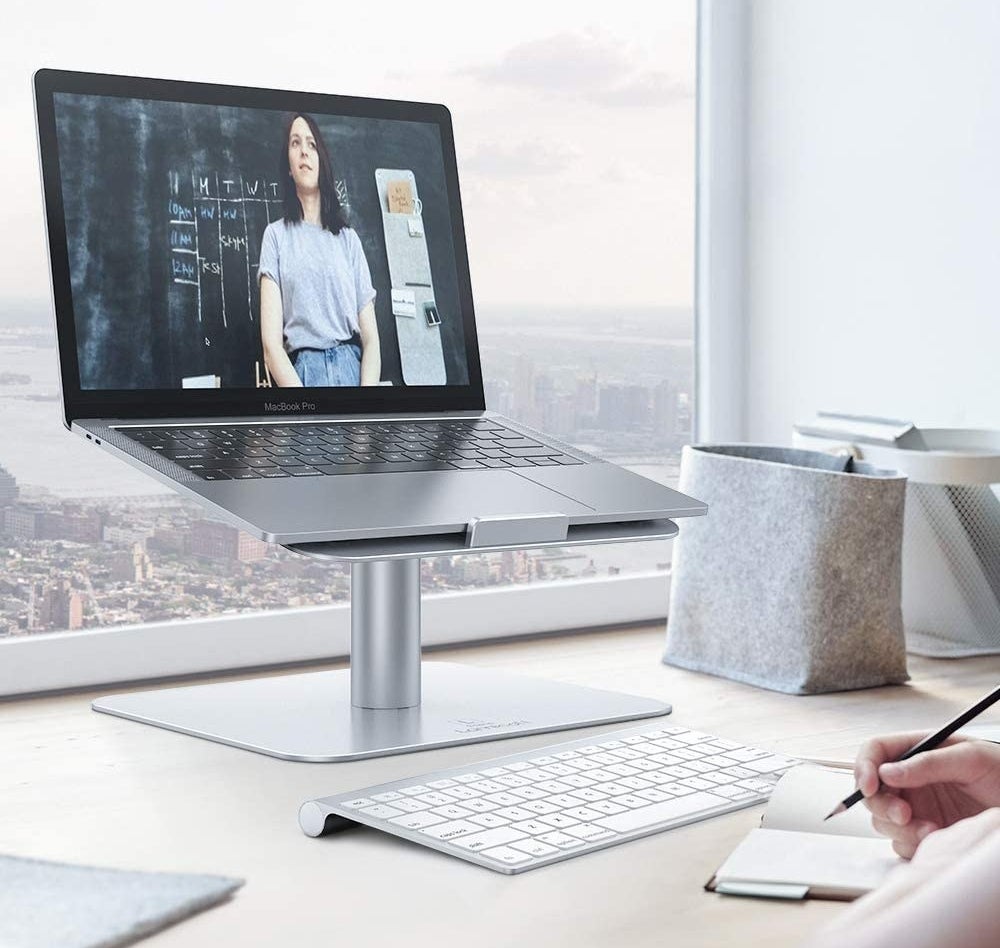 A laptop on the swivel stand in front of a large window with a separate keyboard beneath it 