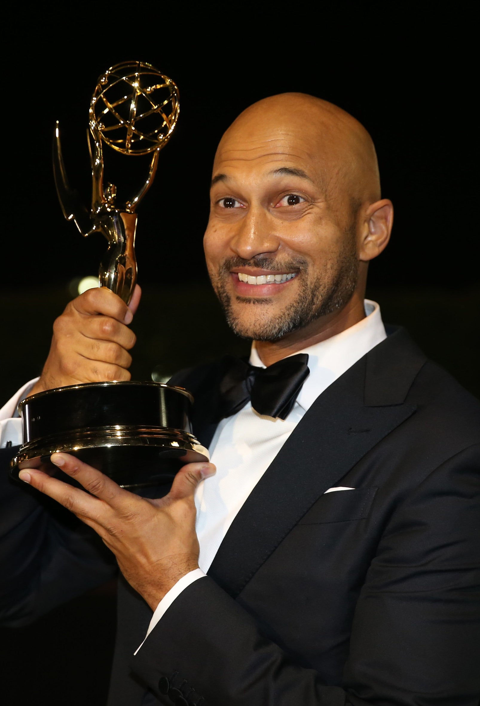 Keegan-Michael Key in a suit, smiling and holding his Emmy Award