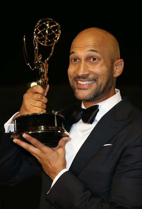 Keegan-Michael Key in a suit, smiling and holding his Emmy Award