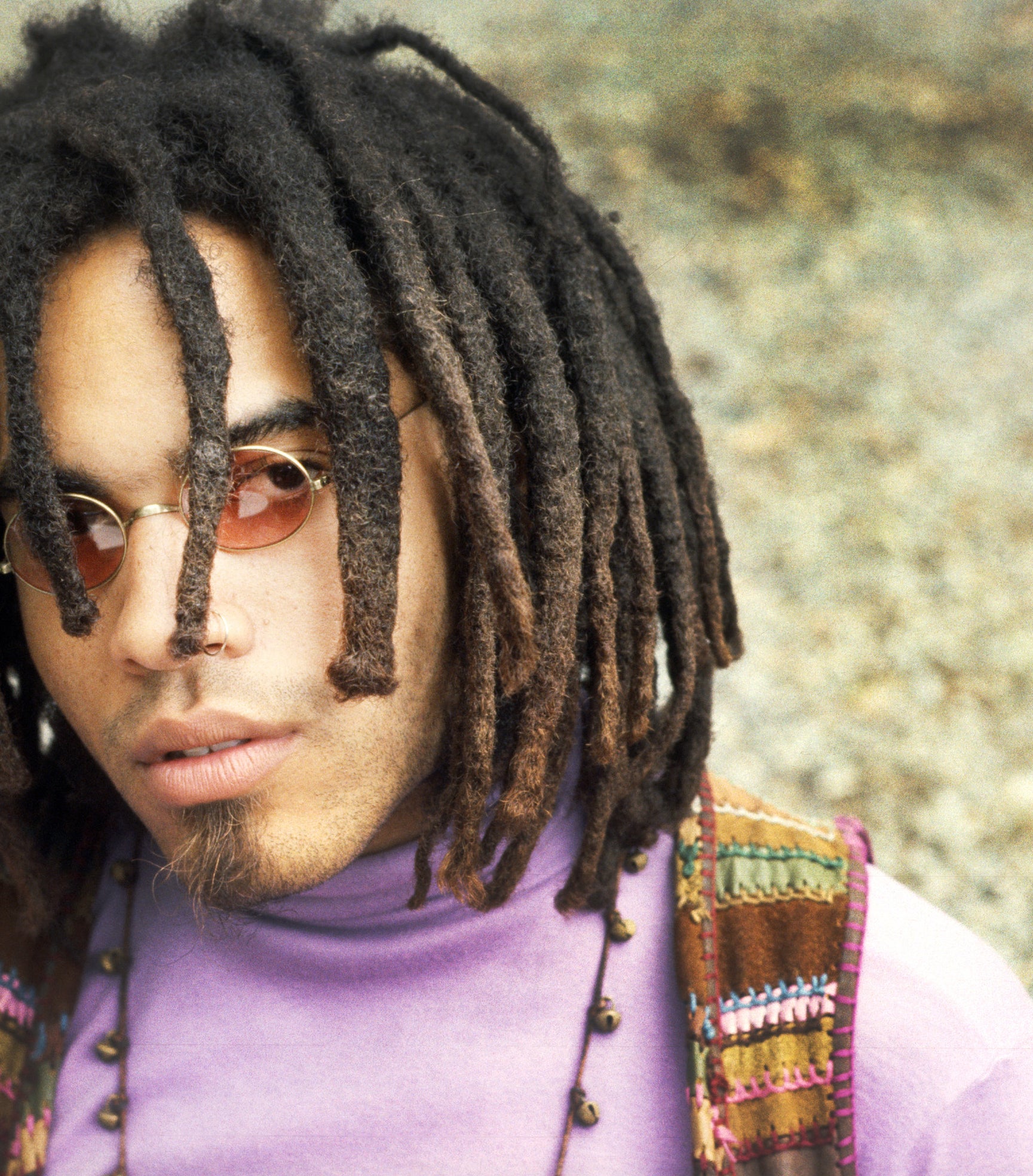 Lenny Kravitz with shorter dreads and sunglasses, wearing a purple turtleneck and striped vest