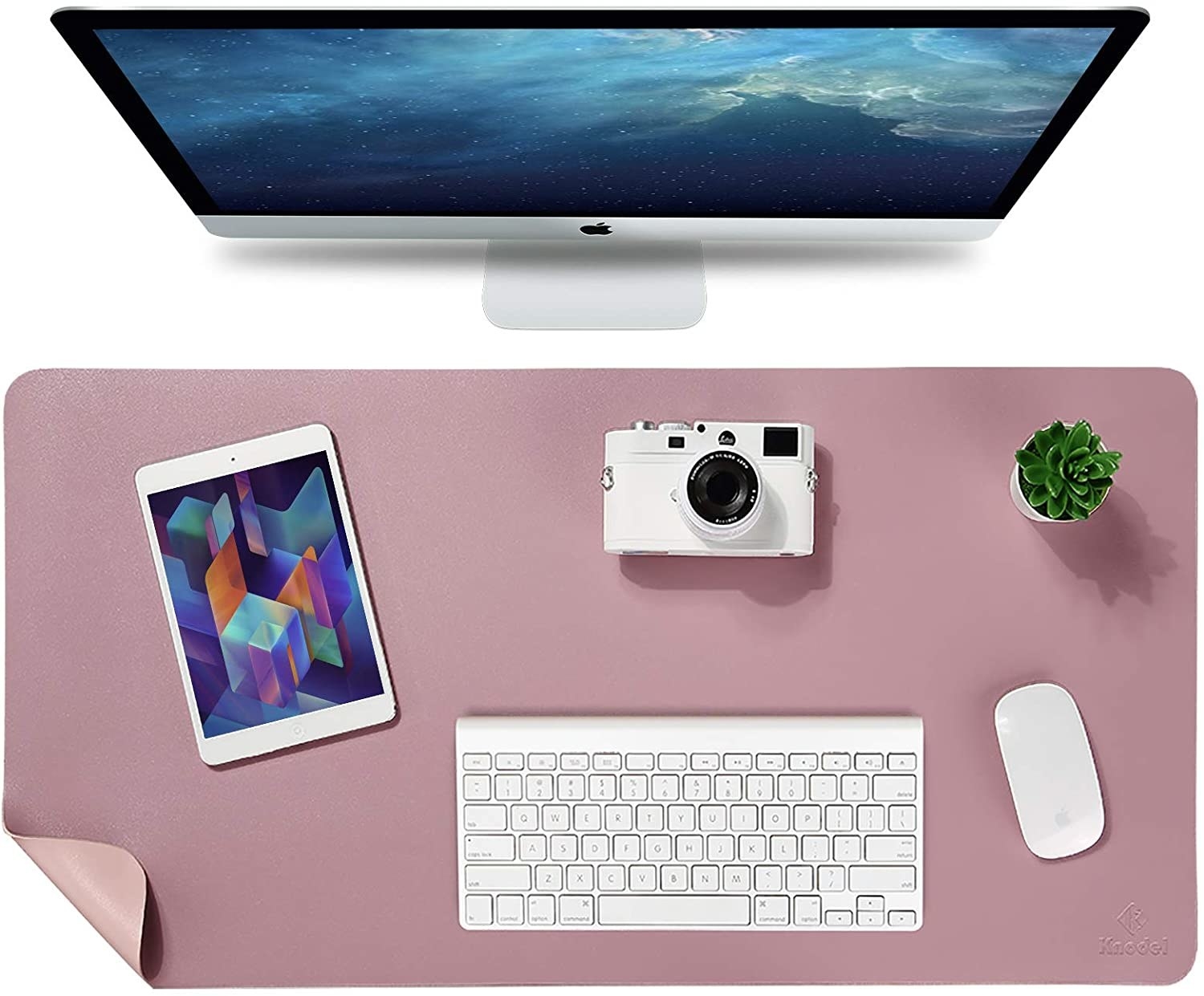The desk mat in front of a monitor with a keyboard, tablet, mouse, plant, and camera on it