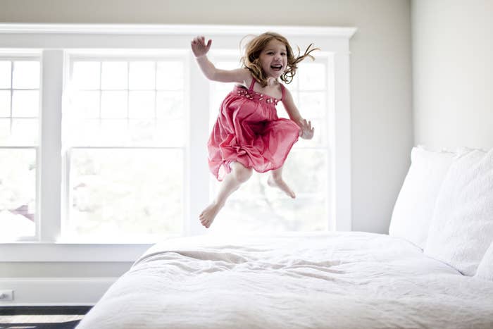Little girl in pink dress jumping on bed