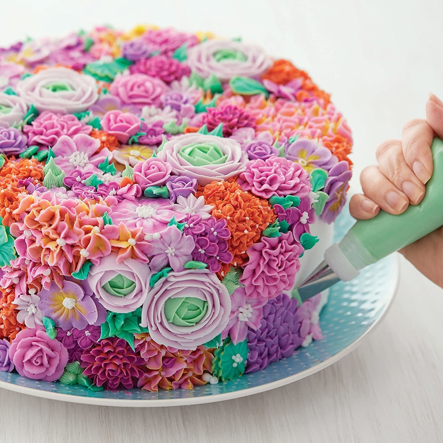 Person decorating cake with multicolored frosting flowers