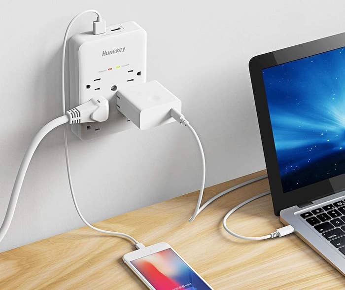 The charging port on a wall above a desk, charging multiple devices simultaneously 