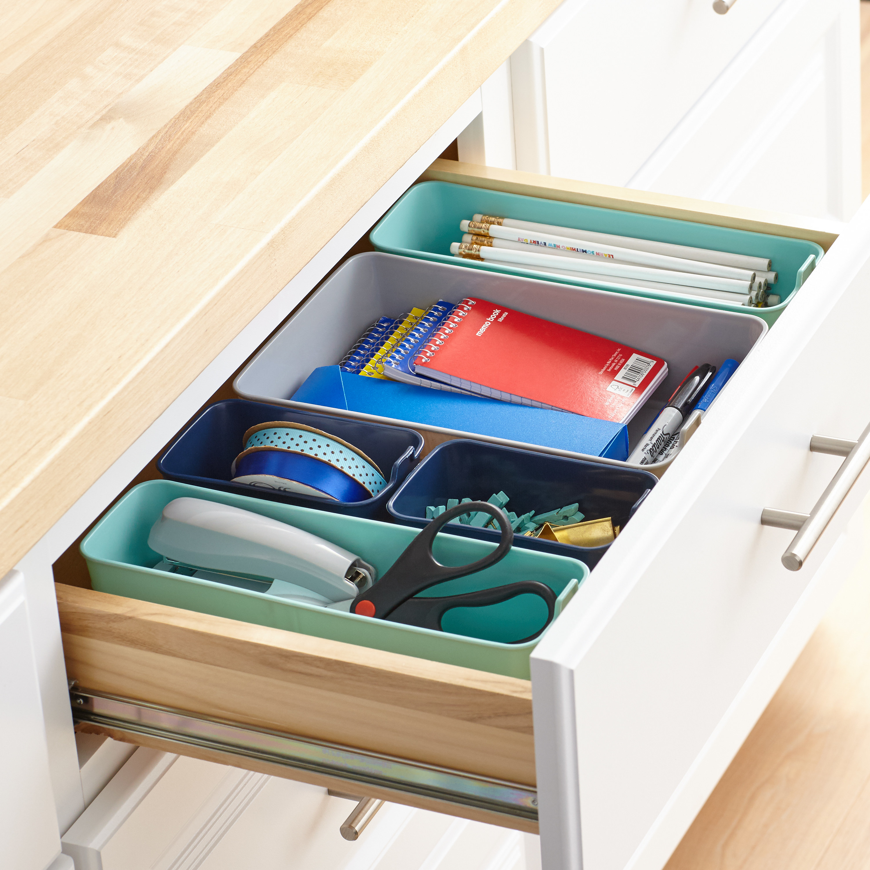 Multi-colored drawer organizers holding various office supplies inside a drawer