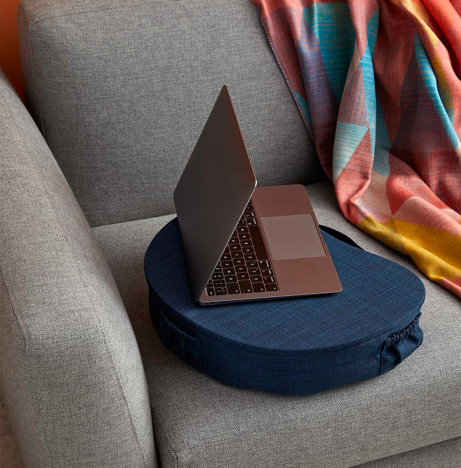 A laptop on the padded laptop table next to a funky blanket