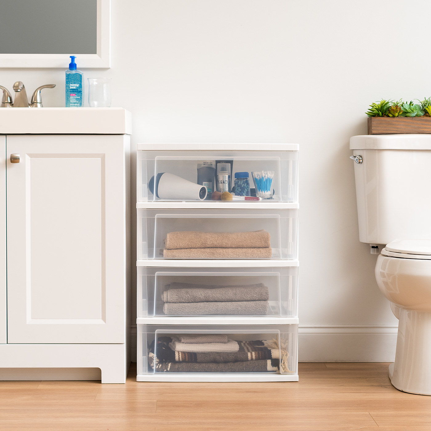 plastic four-drawer storage chest with towels and bath products inside, sitting in a bathroom