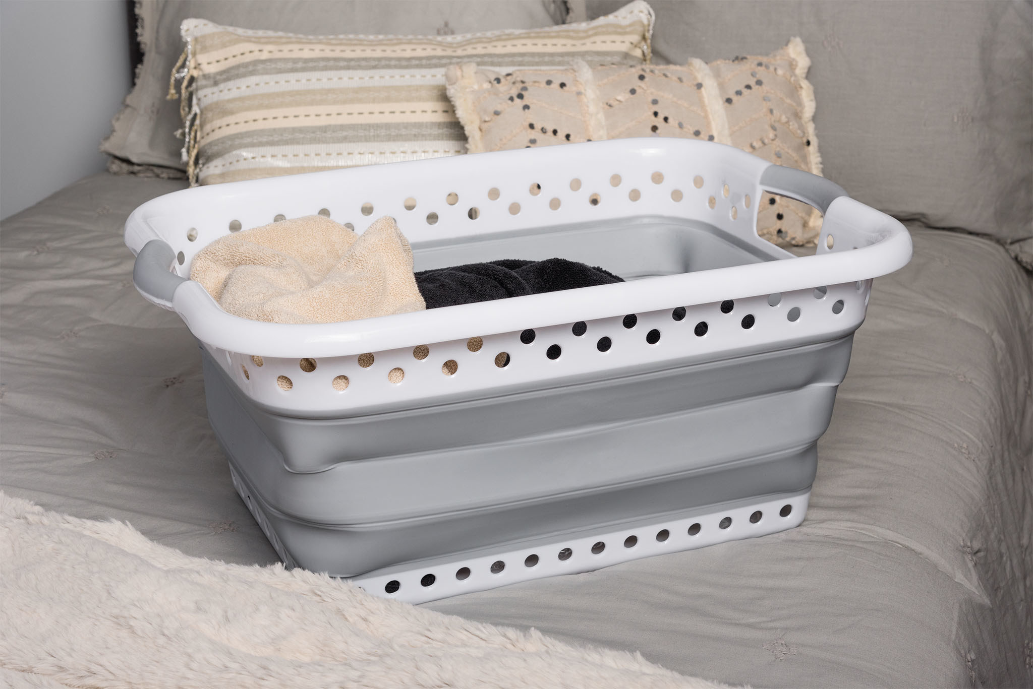 white and gray collapsible laundry basket sitting on a bed