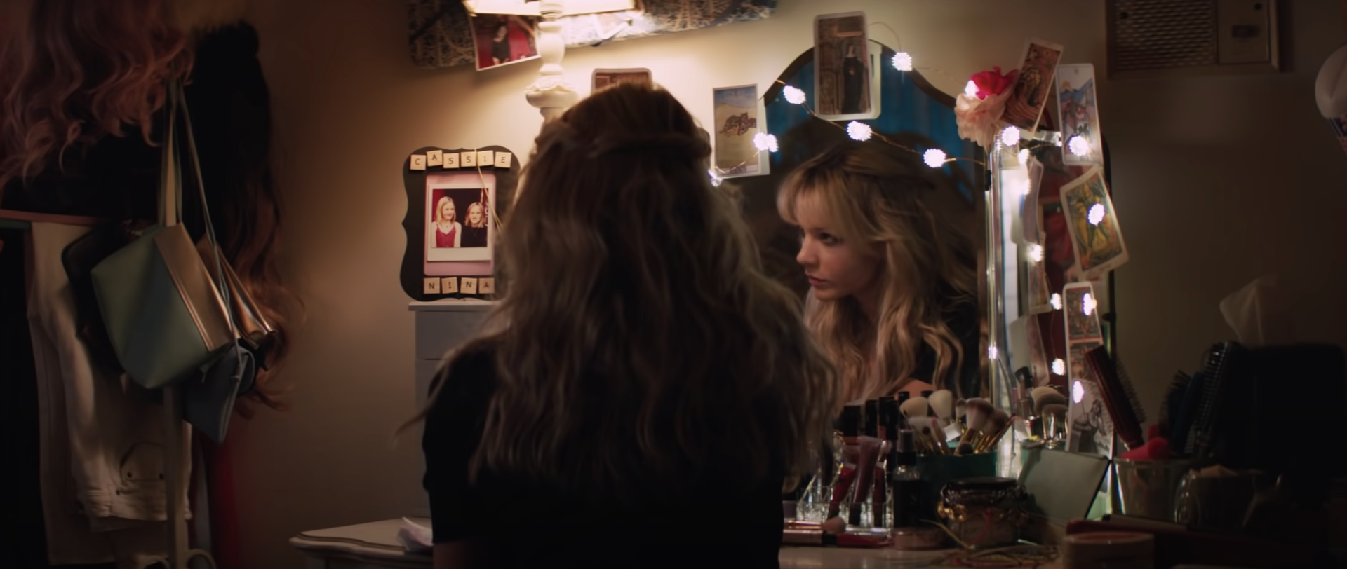 Cassie sitting in front of a mirror decorated with photographs