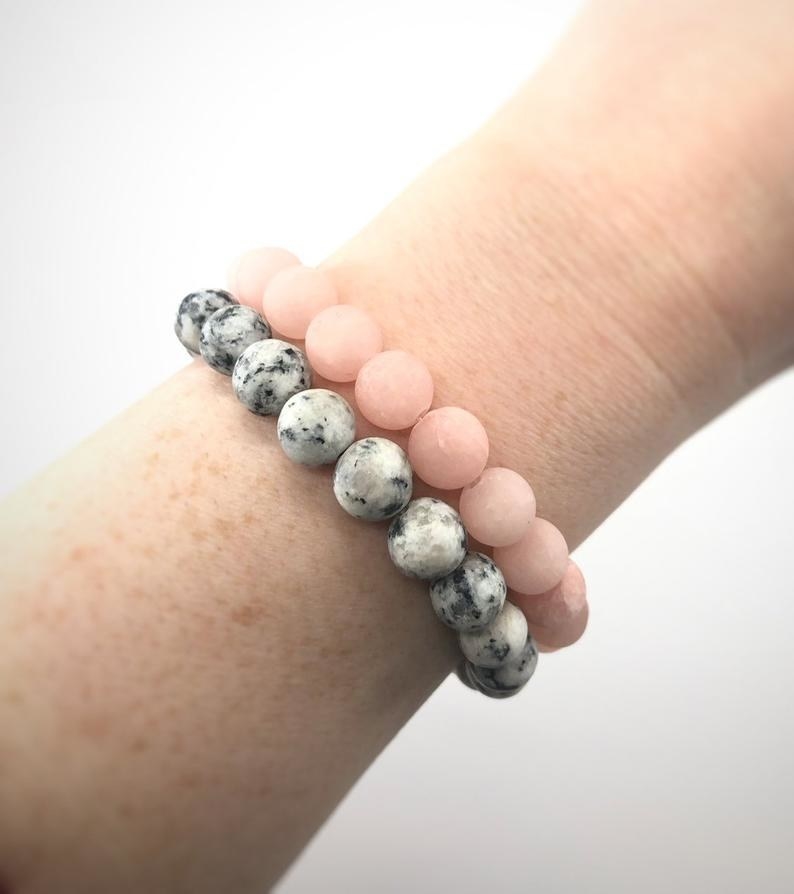 a model wearing a pink beaded bracelet and a marbled gray and black one