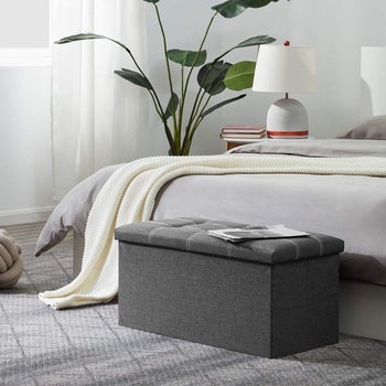gray ottoman at the foot of a bed