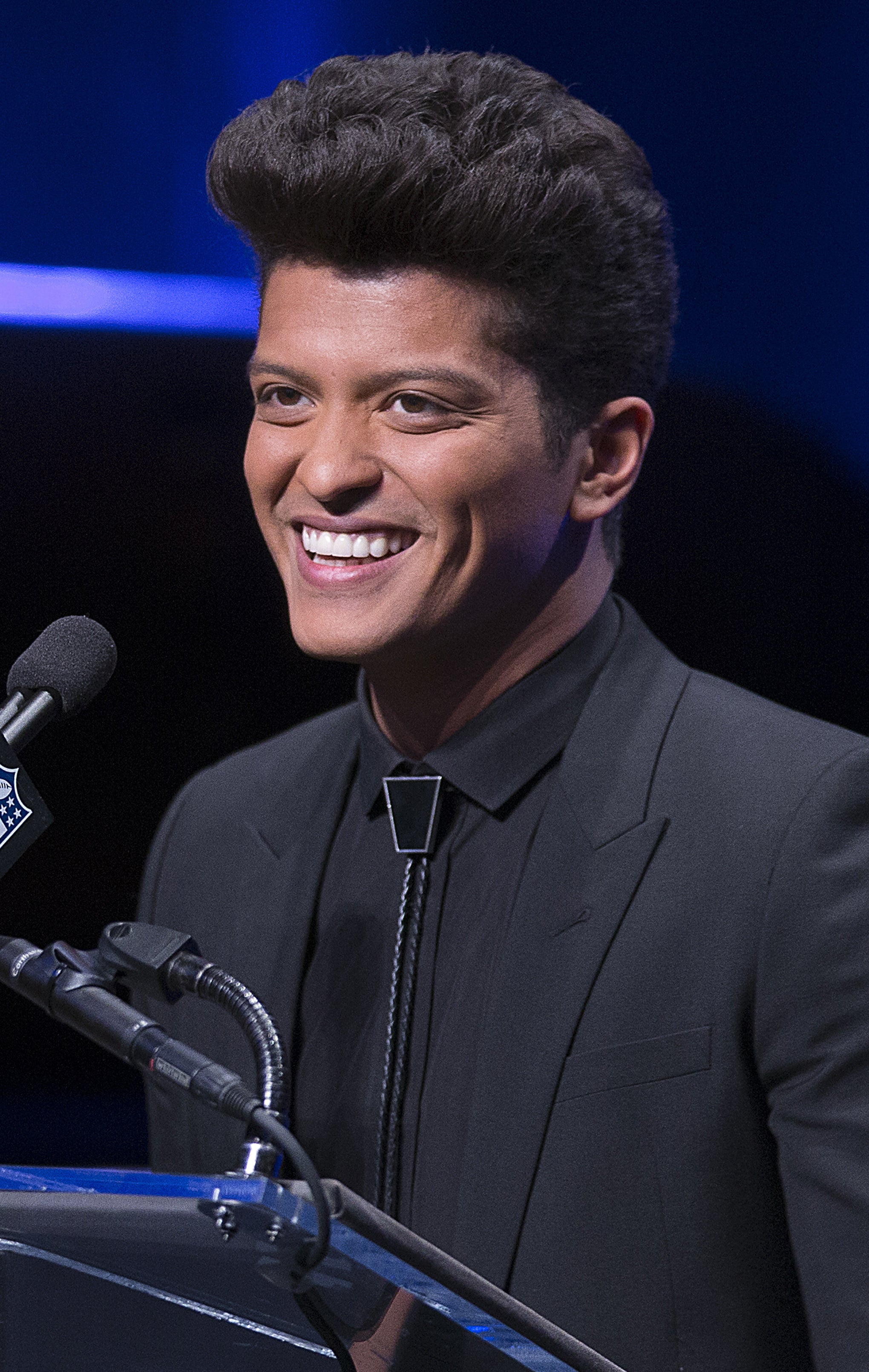 Bruno Mars giving a speech, wearing an all-black suit 