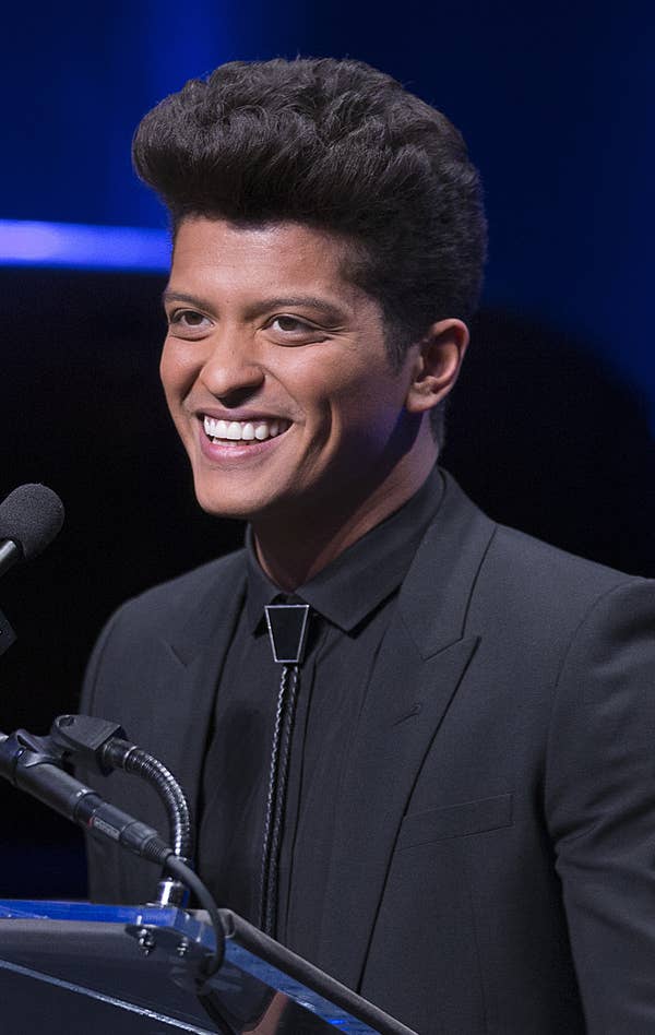 Bruno Mars giving a speech, wearing an all-black suit 