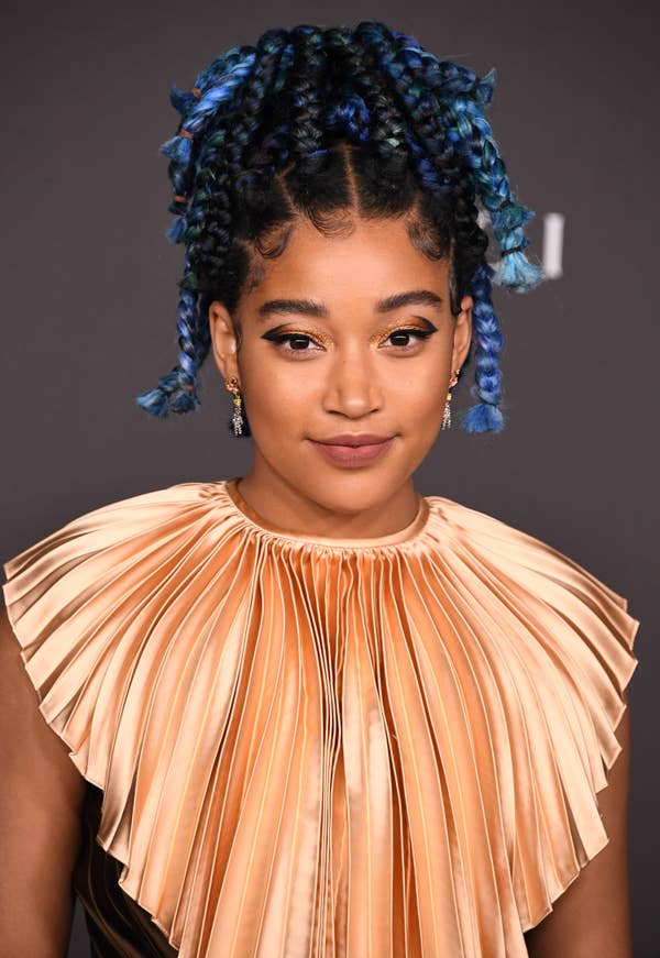 Amandla Stenberg with her hair up in blue braids, wearing a pleated collar-top