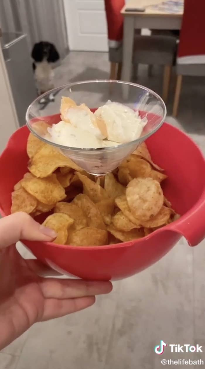 Martini glass filled with dip inside a plastic bowl with chips