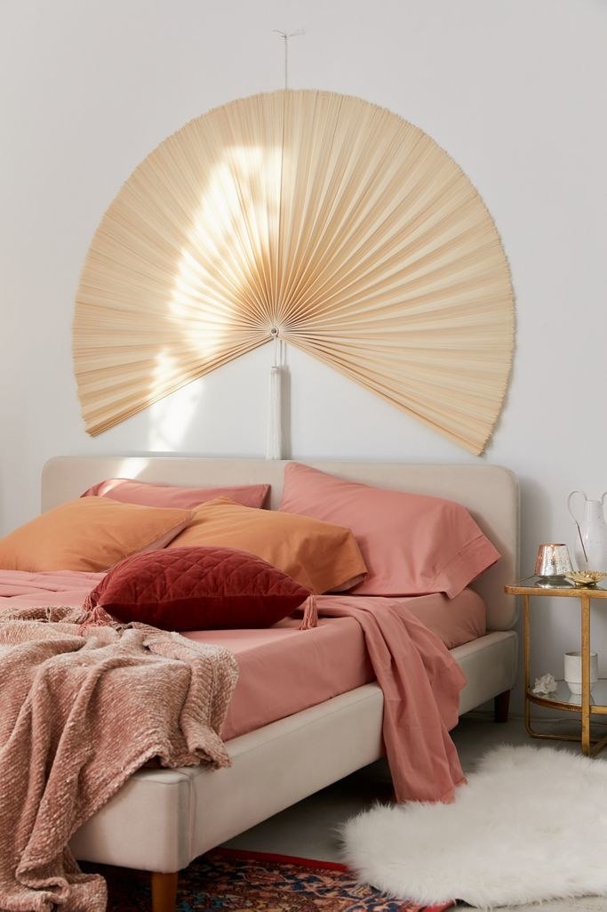 Large beige fan on wall above queen sized bed 