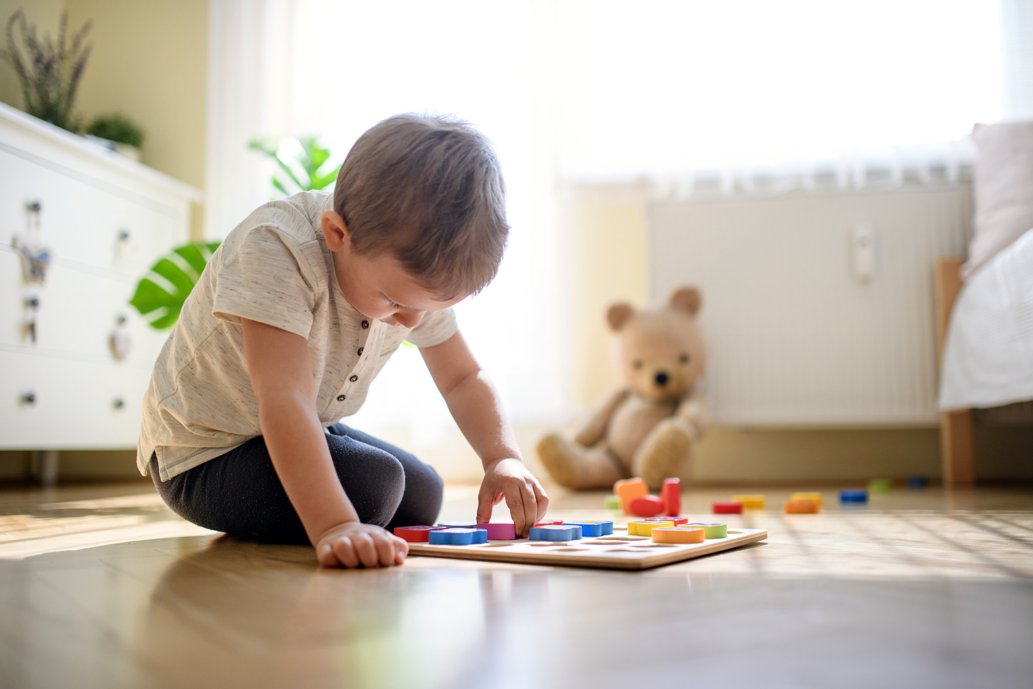 Young boy playing with a puzzle on bedroom floor