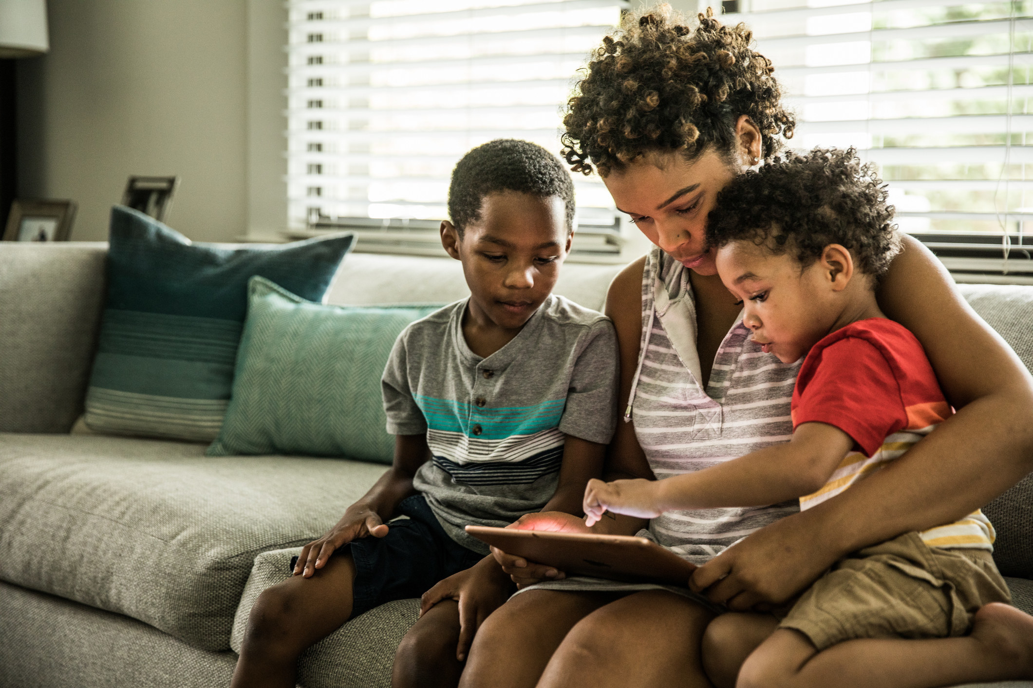 Mother using tablet with two young sons on couch