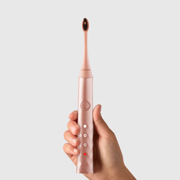 A hand holding the rose gold toothbrush