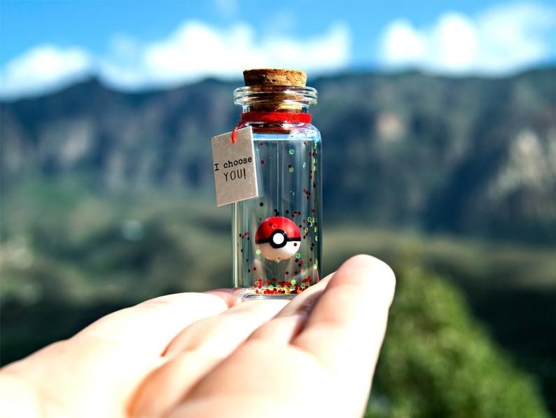 A hand holding the corked bottle with glitter and a Poké Ball that looks like it's floating, with a tag that reads "I choose you!"
