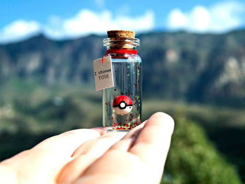 A hand holding the corked bottle with glitter and a Poké Ball that looks like it&#x27;s floating, with a tag that reads &quot;I choose you!&quot;