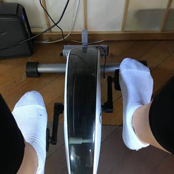 A top-down reviewer photo of someone wearing socks and using the under-desk bike