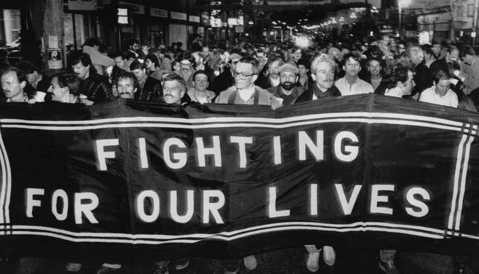 Hundreds of men protest, holding up a large sign that says "Fighting For Our Lives"
