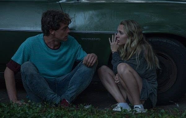 Broussard and Iseman crouching down on the ground while leaning against the side of a car