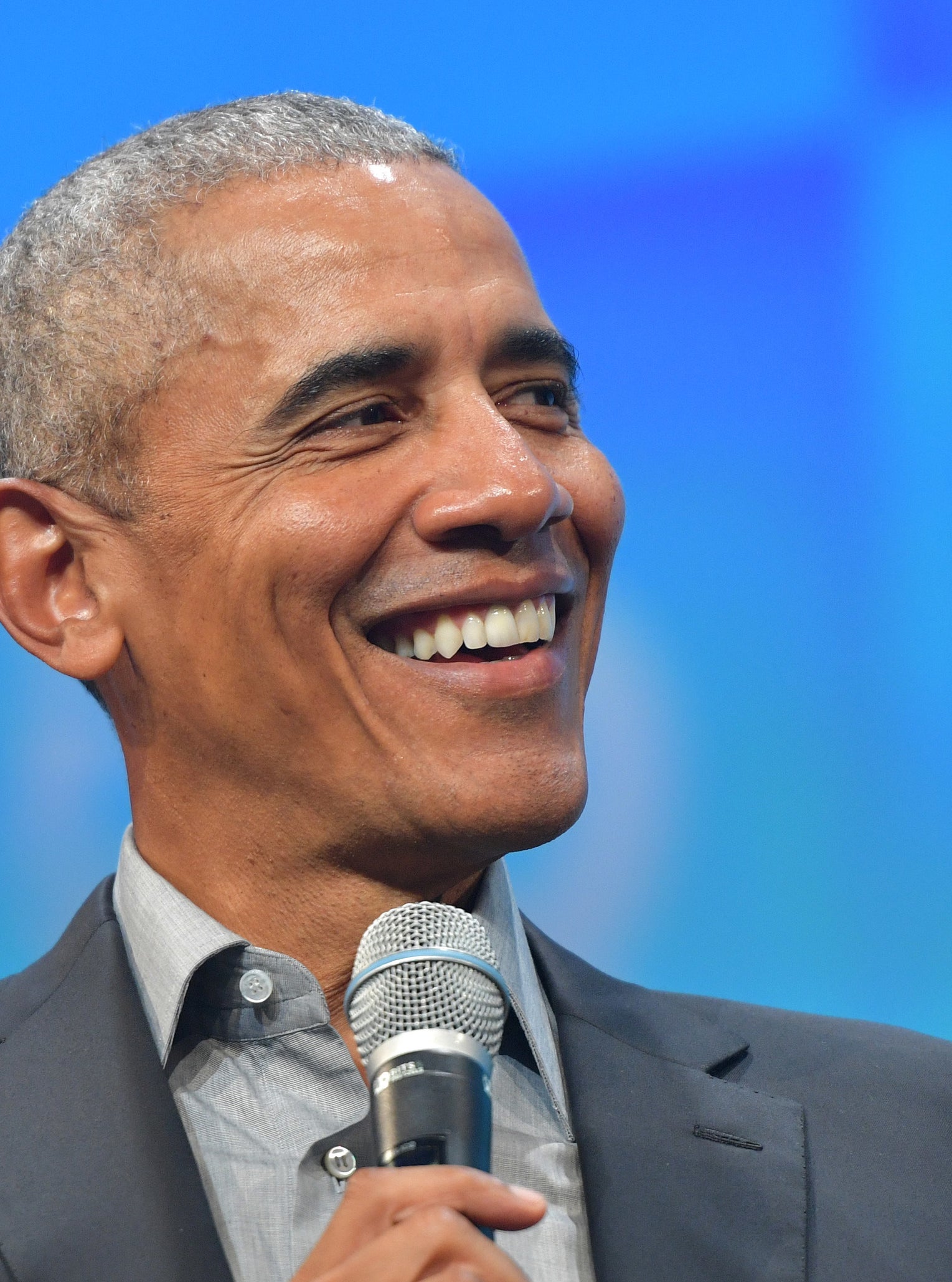 President Obama smiling as he holds a mic, wearing a suit