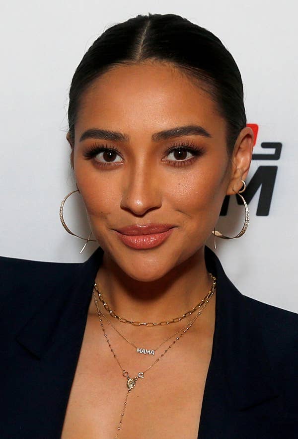 Shay Mitchell with her hair slicked back into a bun, wearing a blazer as she smiles at the camera