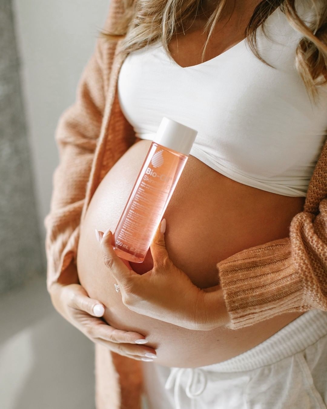 A person holding a bottle of Bio-Oil next to their bump