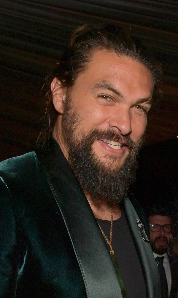 Jason Momoa smiling with his hair pulled back into a bun and a green, velvet suit