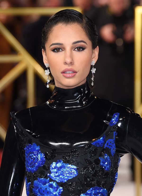 Naomi Scott looks into the camera at a Charlie&#x27;s Angels event, wearing a latex black turtleneck and sequenced blue and black dress