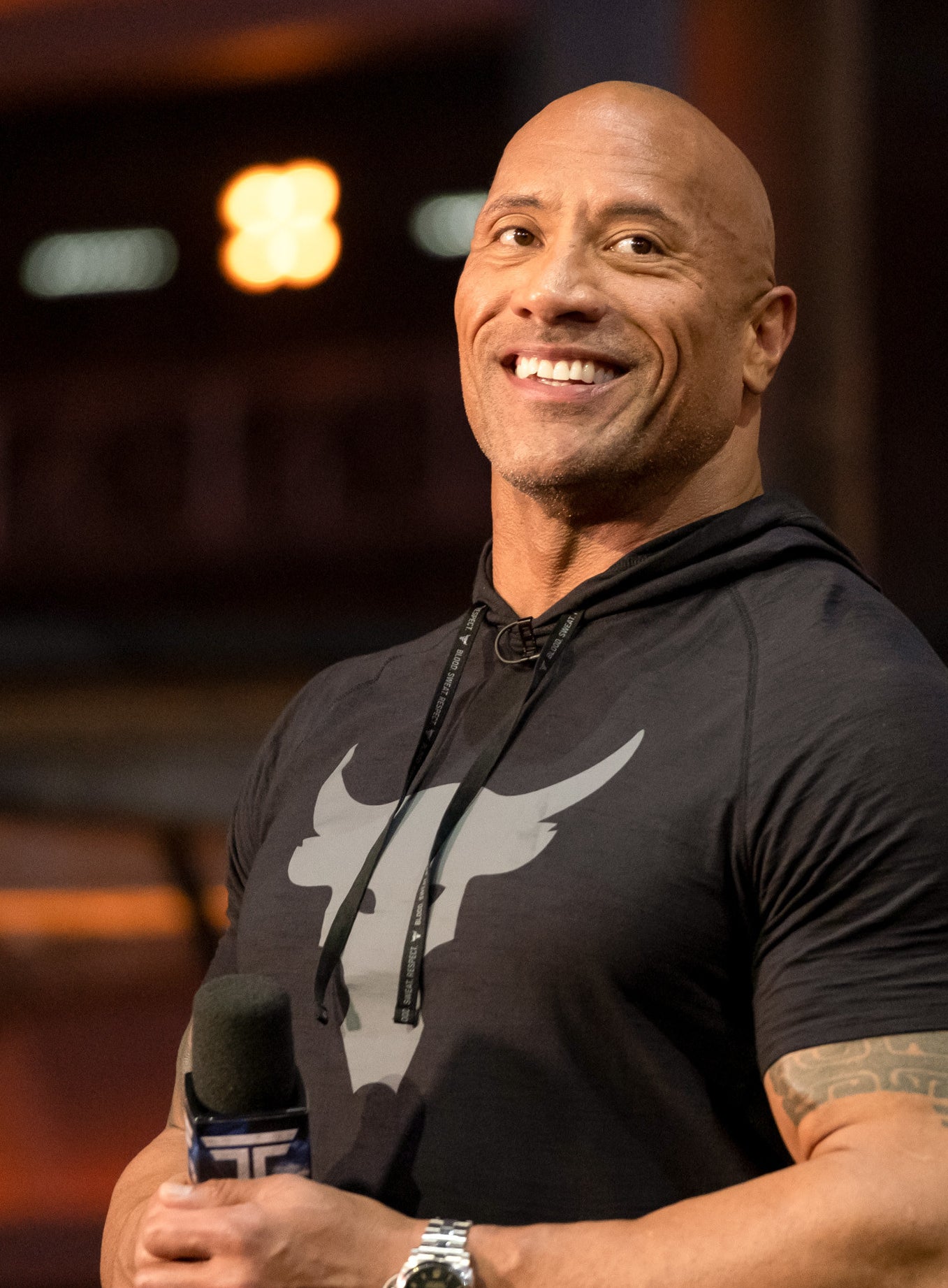 The Rock smiling as he hosts &#x27;The Titans Games&#x27; in a black, Under Armour, short-sleeved hoodie