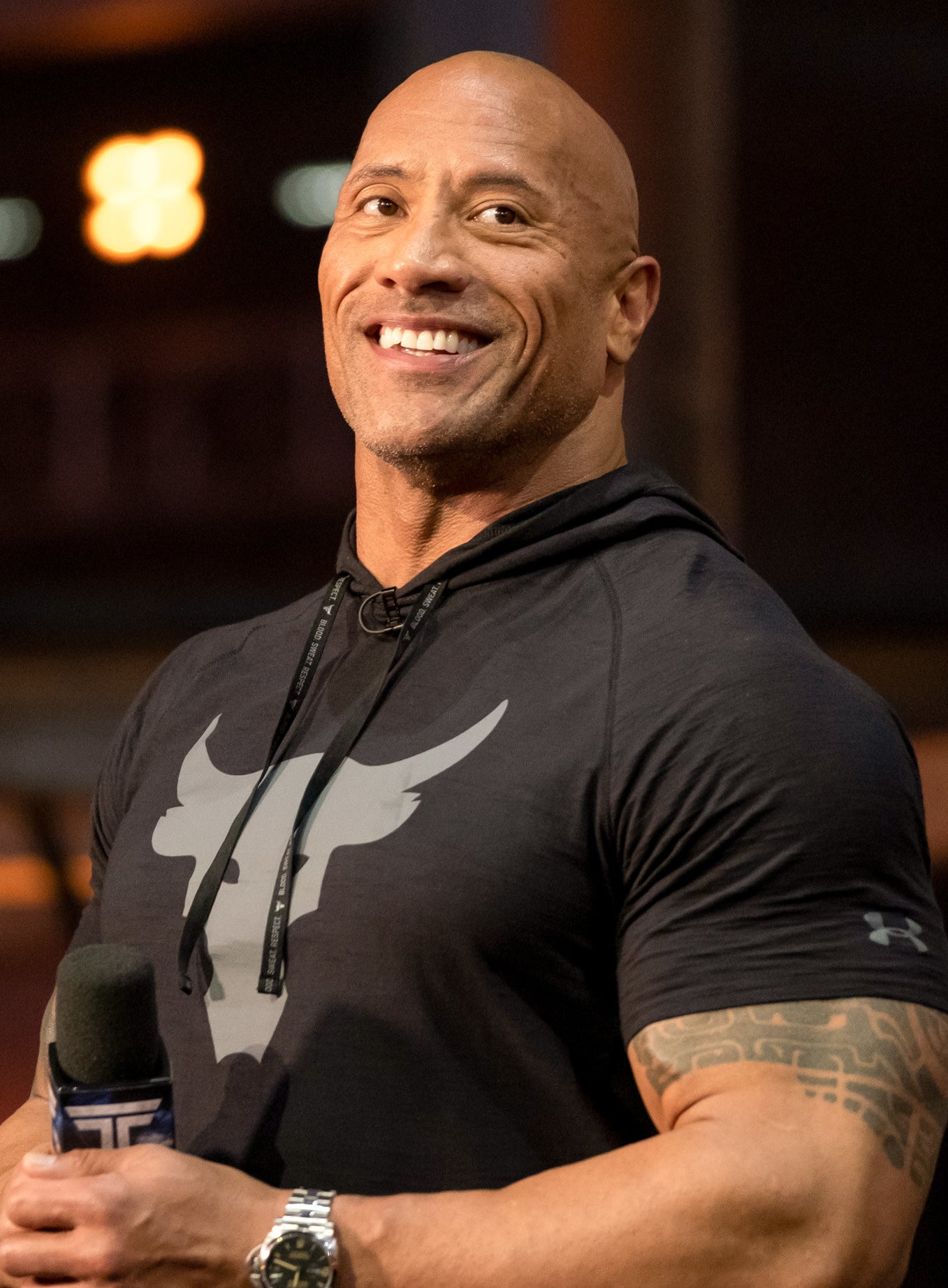 The Rock smiling as he hosts &#x27;The Titans Games&#x27; in a black, Under Armour, short-sleeved hoodie