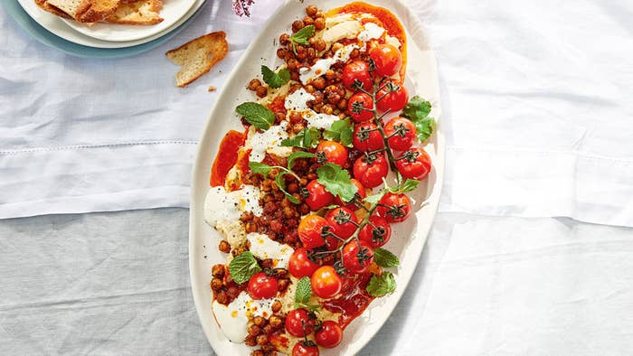 Oval platter filled with hommus that had vine tomatoes, garnish and roasted chickpeas